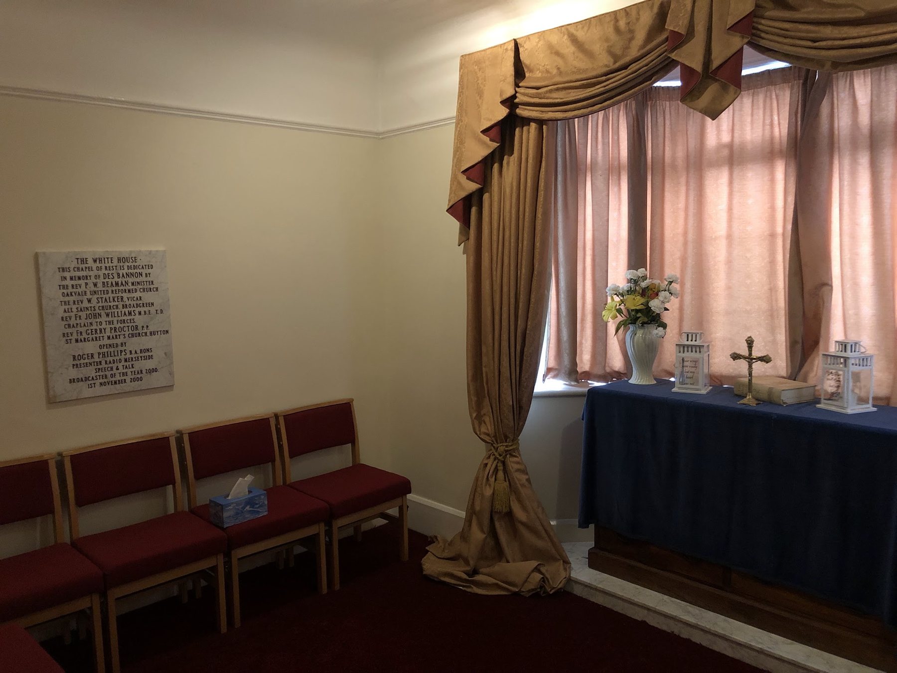 A chapel of rest with red chairs, gold-trimmed curtains and a draped altar table