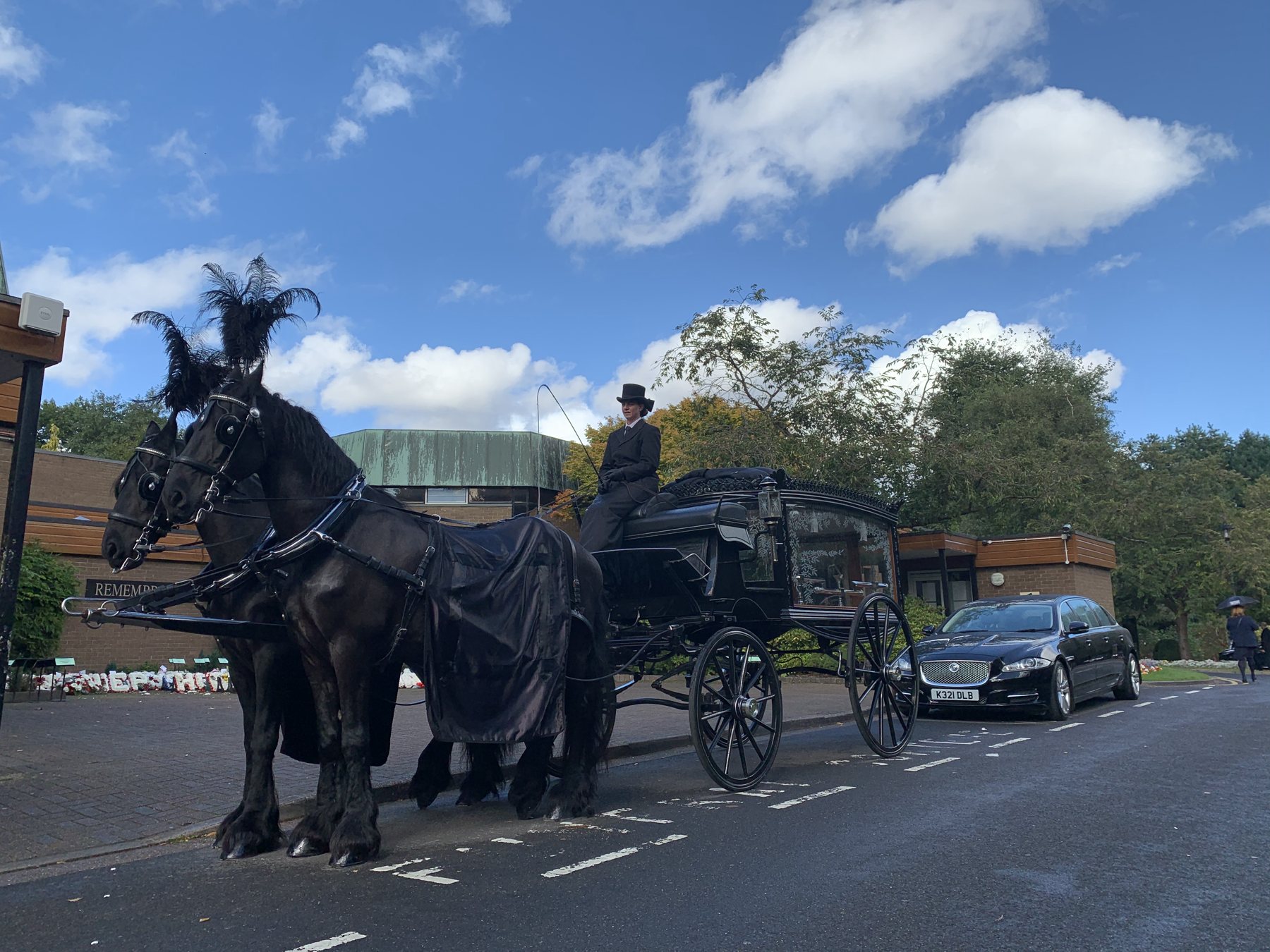Black horses drawing a glass hearse along a road