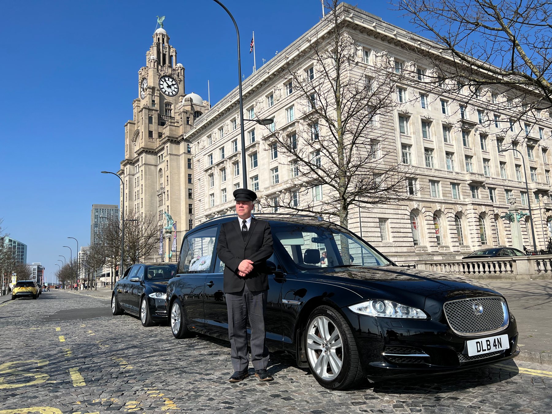 A Jaguar hearse with its driver beside the Liver Building